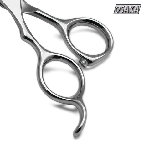 Gros plan sur le manche inversé des ciseaux OSAKA GXL gaucher – repose-doigt courbé allongé et anneaux ergonomiques symétriques en finition acier poli
