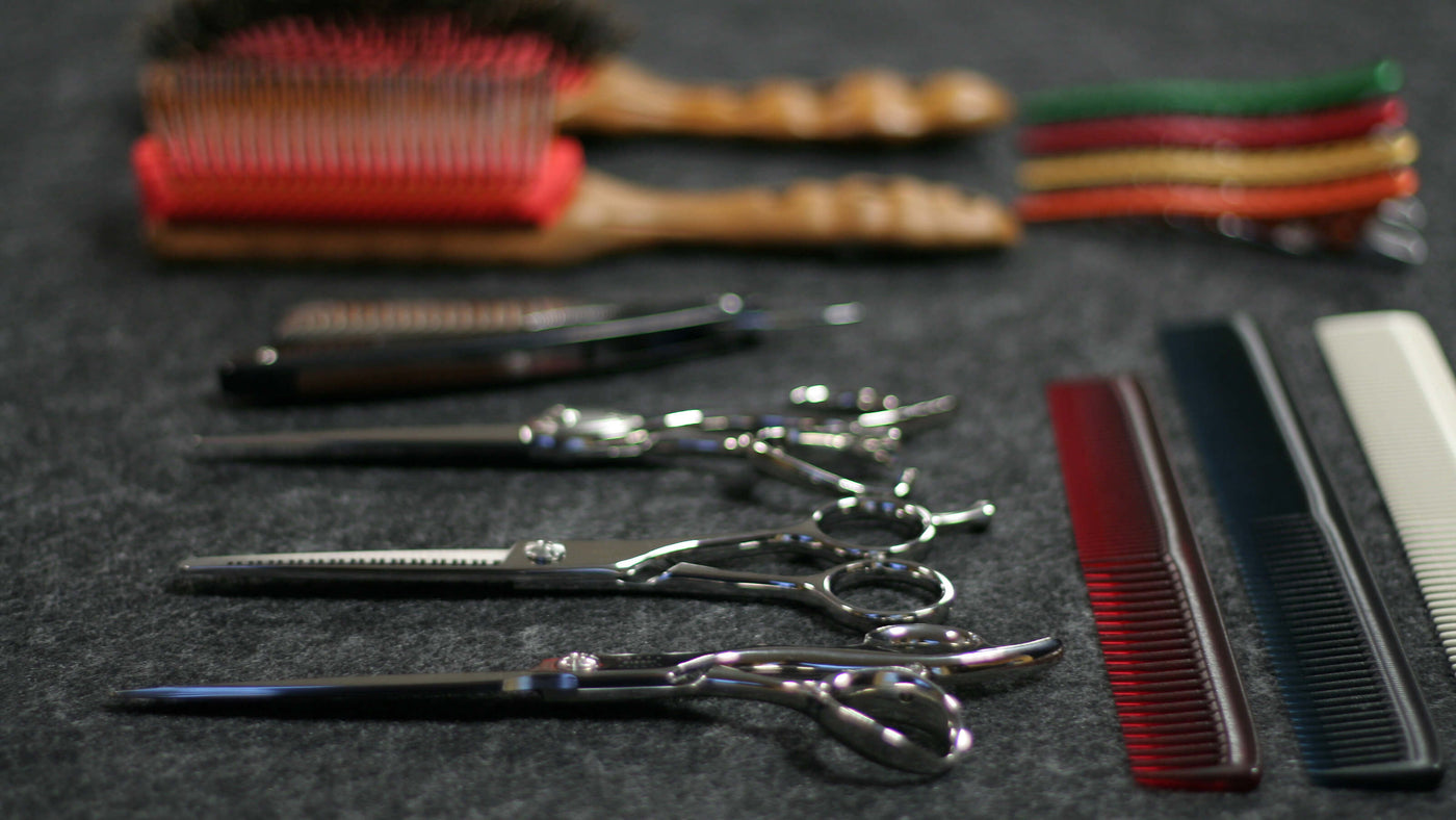 3 paires de ciseaux kissei de coiffure professionnels posés à côtés de brosses ou de peignes de coupes en arrière plan 